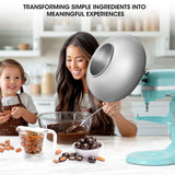 Woman and child in a kitchen preparing food with a mixer, surrounded by ingredients.
